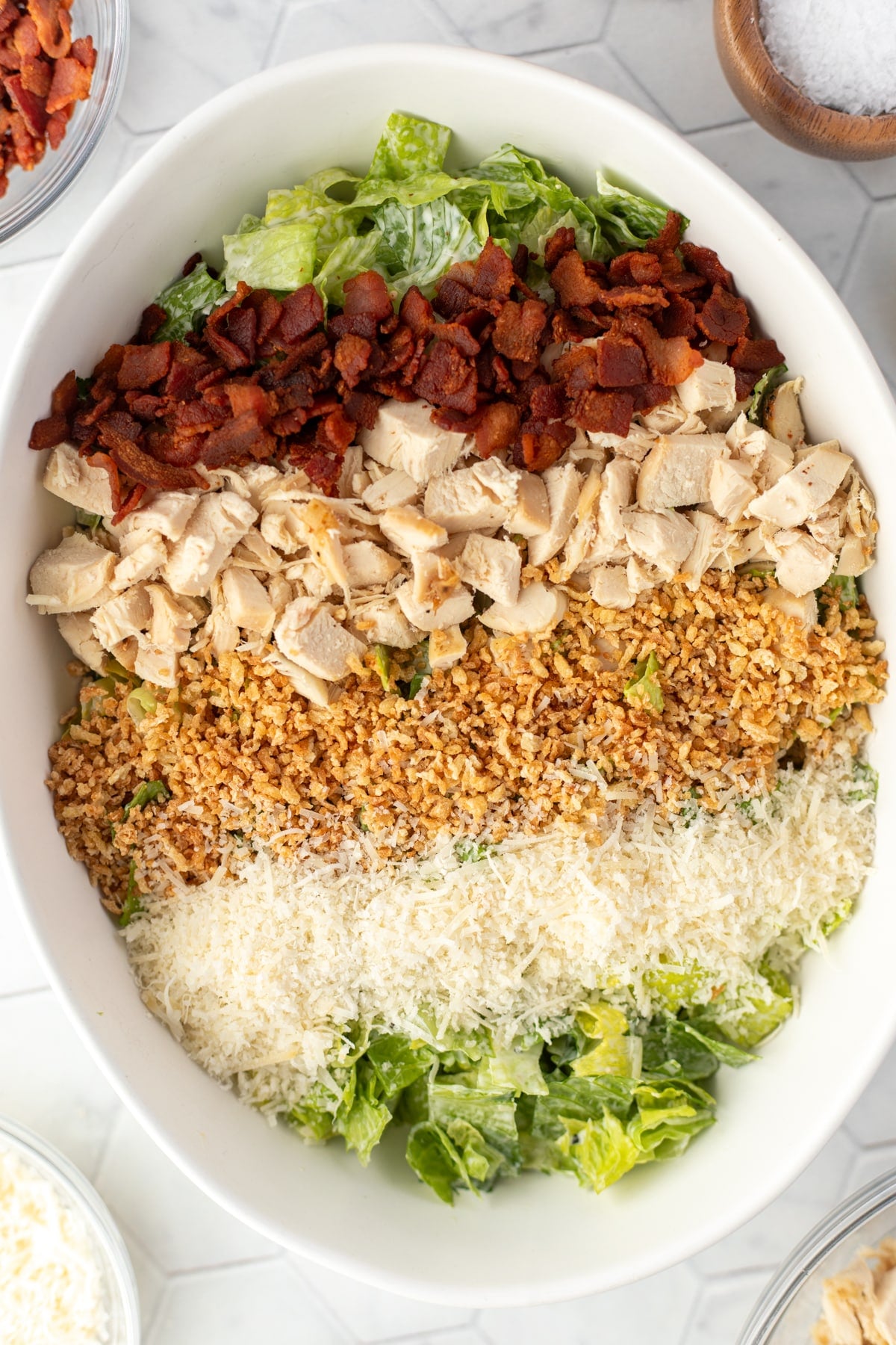 A bowl of dressed romaine with parmesan, toasted breadcrumbs, chicken, and bacon.