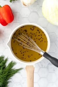 Whisking together a brine with peppercorns in a small saucepan.