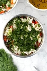 A large pot filled with chopped vegetables, dill, and parsley.