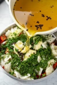 Pouring brine over cabbage, dill, parsley, and vegetables.