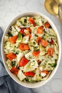 A bowl filled with marinated cabbage salad, featuring red pepper and dill.