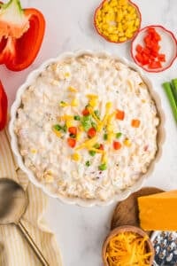 A bowl of corn dip topped with chopped bell pepper, green onion, and cheese.
