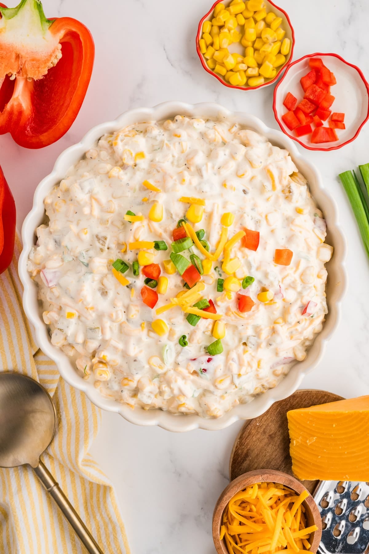 A bowl of corn dip topped with chopped bell pepper, green onion, and cheese.