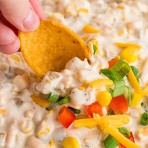 Dipping a frito corn chip into a creamy corn dip with bell pepper, corn, and cheese.