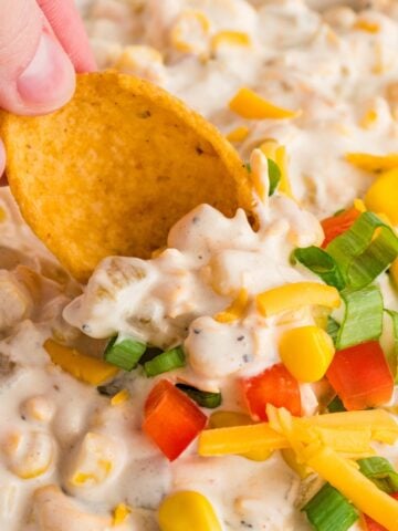 Dipping a frito corn chip into a creamy corn dip with bell pepper, corn, and cheese.