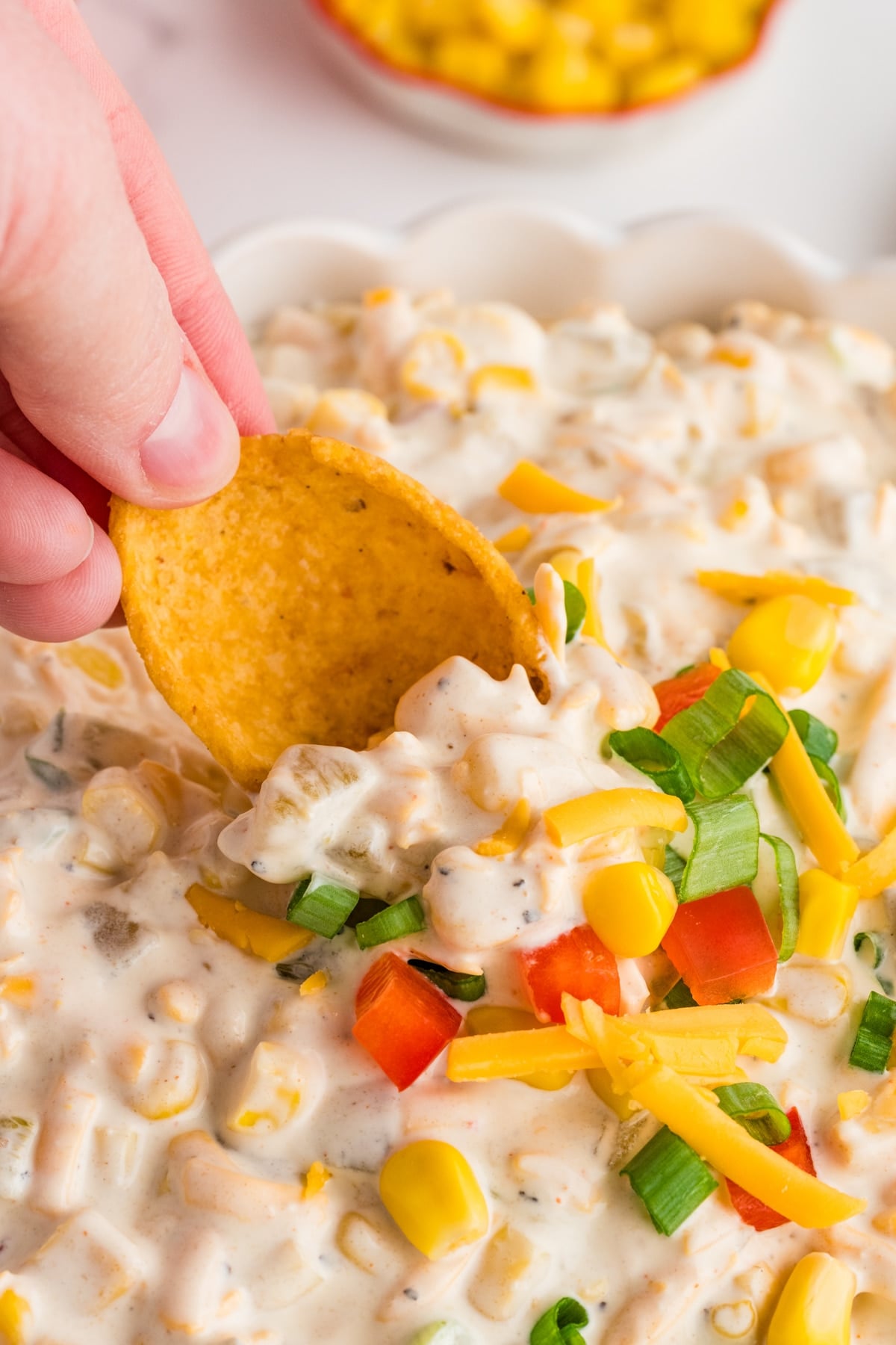 Dipping a corn chip into a bowl of creamy dip with bell pepper, cheese, and green onion.