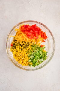 A bowl with corn, cheese, bell pepper, green onion, and green chiles on top of a cream dip base.
