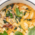 A soup pot full of creamy soup with tortellini, basil, and sundried tomato.