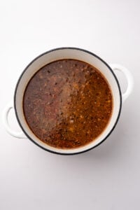 A soup base with a dark color, with aromatics floating subtly.