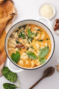 A soup pot filled with tender tortellini, a creamy broth, and topped with fresh basil.
