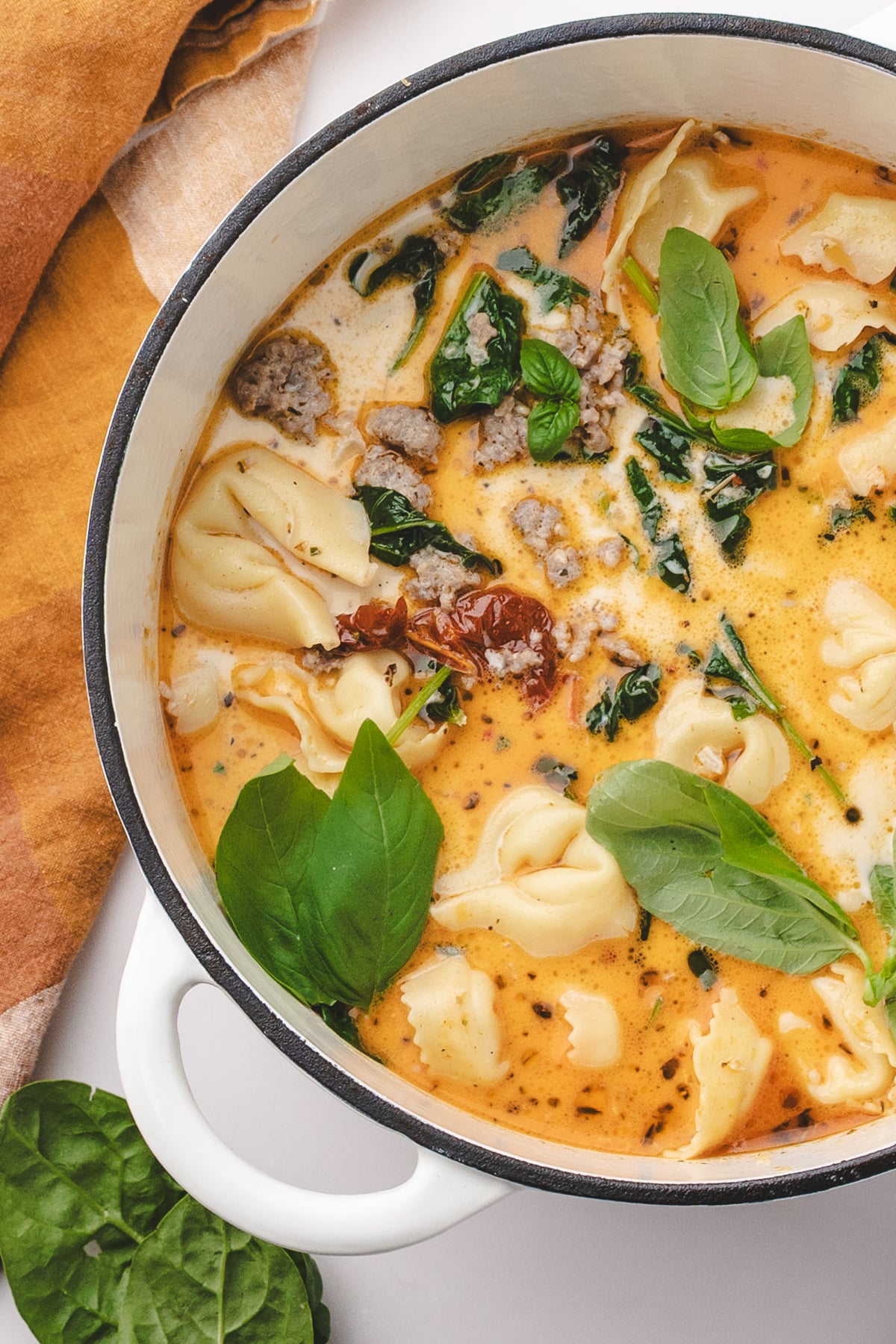 A Dutch oven filled with creamy tuscan soup, featuring tortellini and fresh basil.