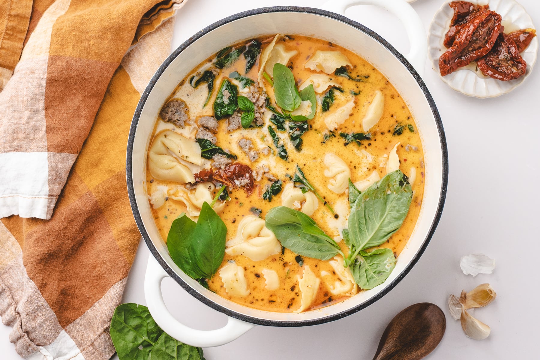 A Dutch oven filled with soup, featuring a creamy broth, tortellini, basil, and sundried tomatoes.