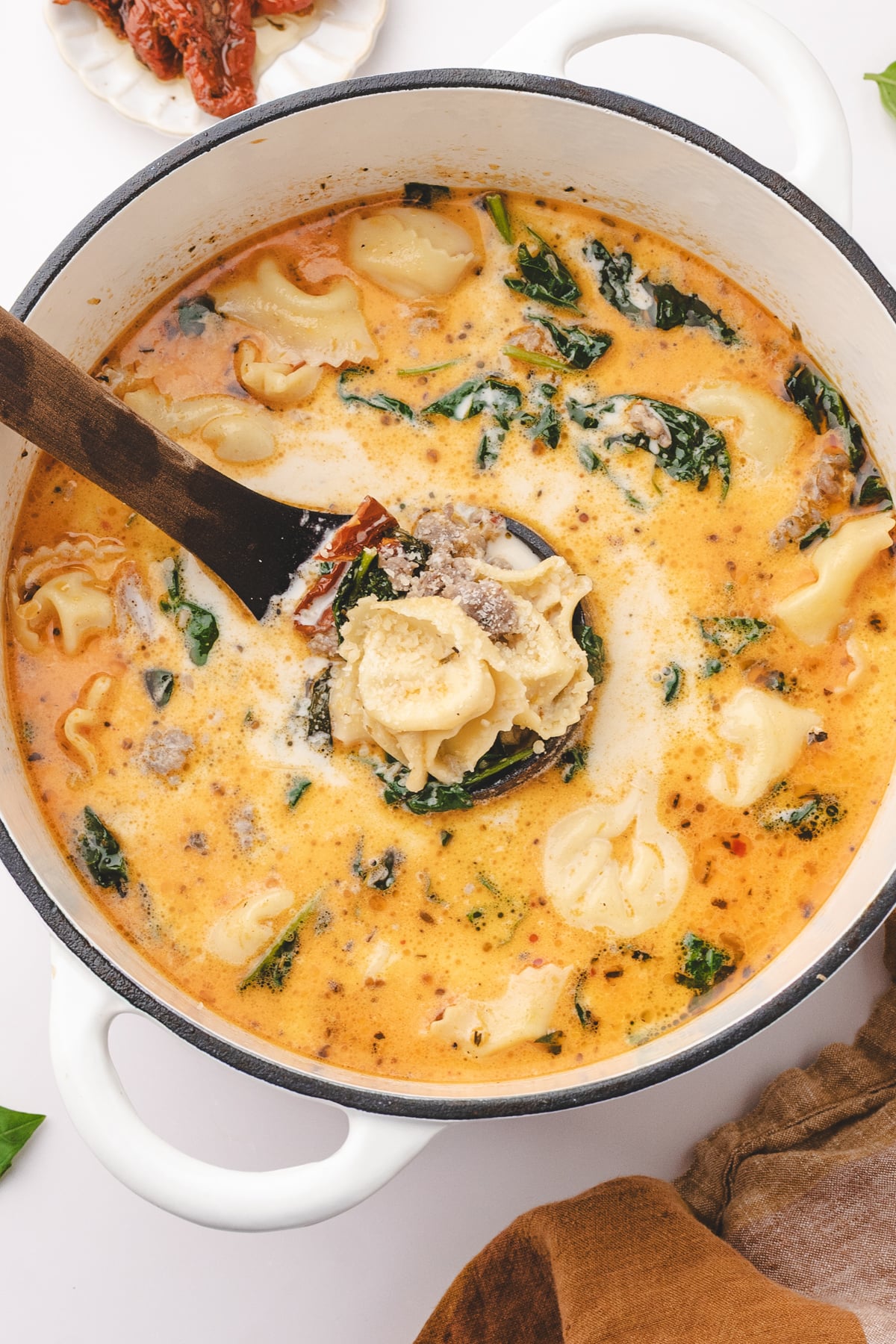 Taking a ladleful of tortellini soup from a Dutch oven.