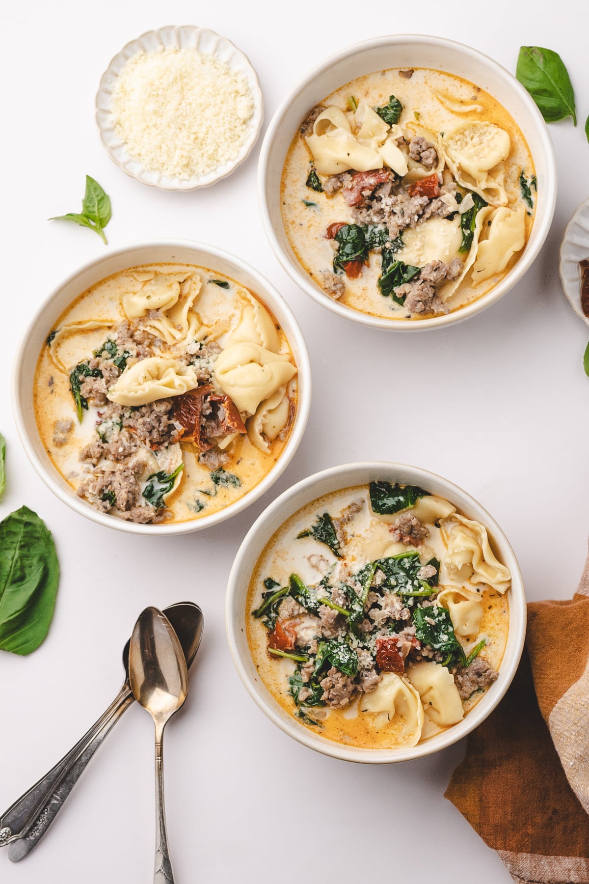 Several bowls of creamy soup with tortellini, spinach, and basil.