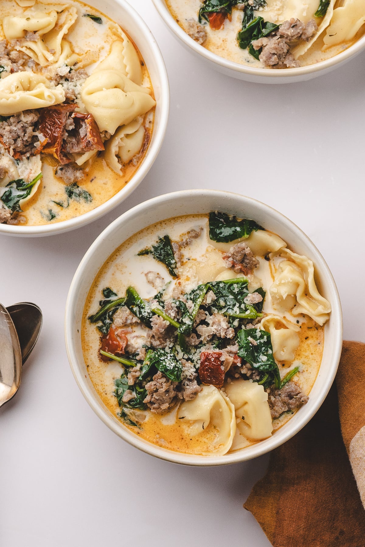 A bowl of soup with creamy broth, tortellini, spinach, and sausage.