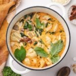 A Dutch oven filled with creamy soup, featuring tortellini, sausage, and fresh basil.