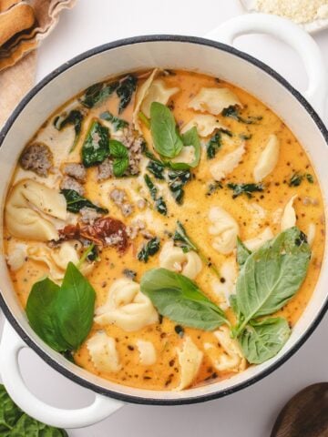 A Dutch oven filled with creamy soup, featuring tortellini, sausage, and fresh basil.