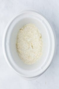 A cream cheese mixture in the bottom of a slow cooker insert.