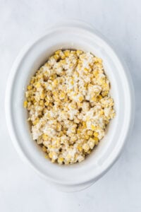 Corn kernels coated in a creamy mixture in a slow cooker.
