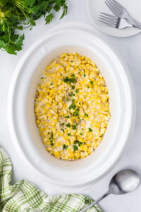 A slow cooker insert filled with creamy corn and topped with fresh parsley.